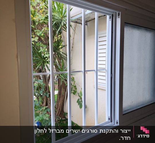 חלון עם סורגים לבנים וצמחייה בחוץ